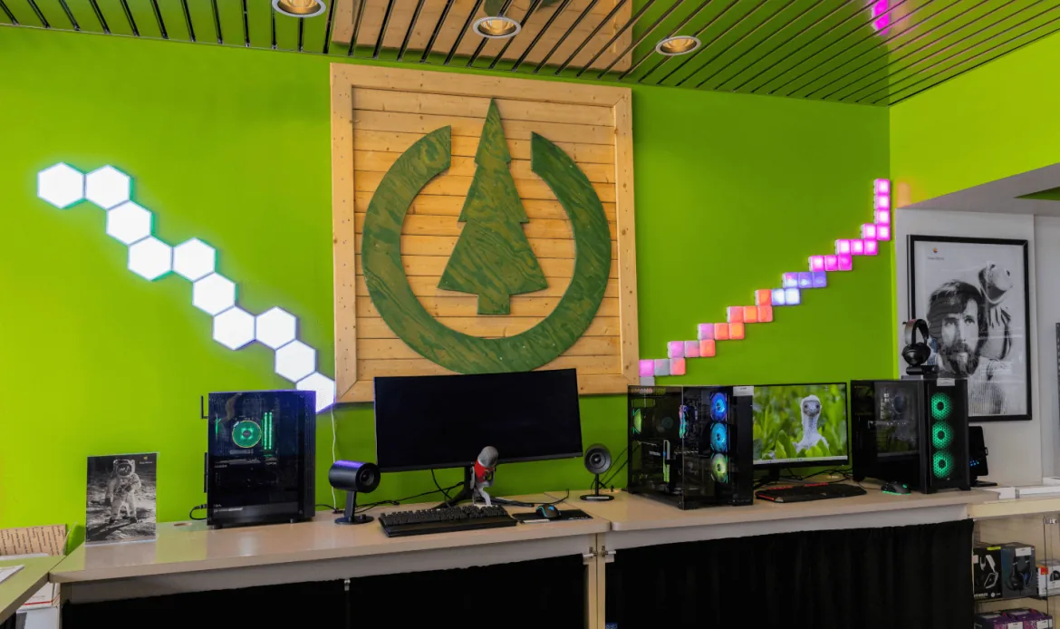Three custom-built gaming PCs with RGB lighting on the counter beneath the wooden Computer Doctor logo on a green wall
